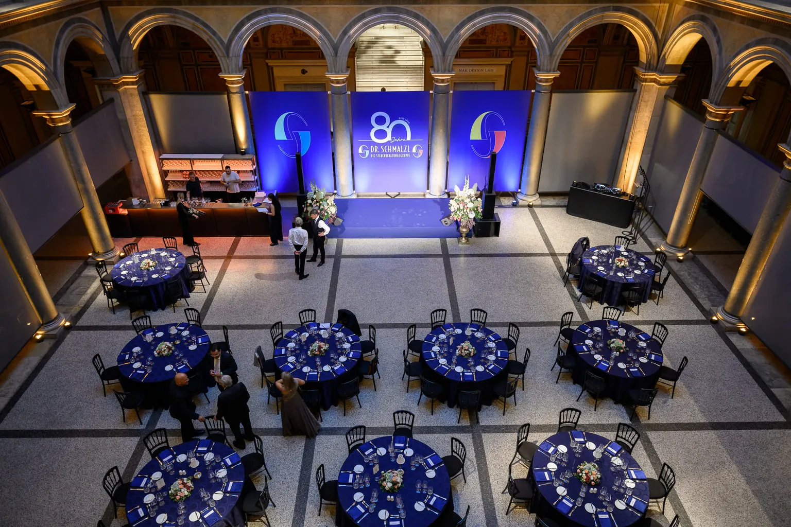 Blick von oben auf die Säulenhalle im MAK mit blau gedeckten Tafeln und der Jubiläumsbühne