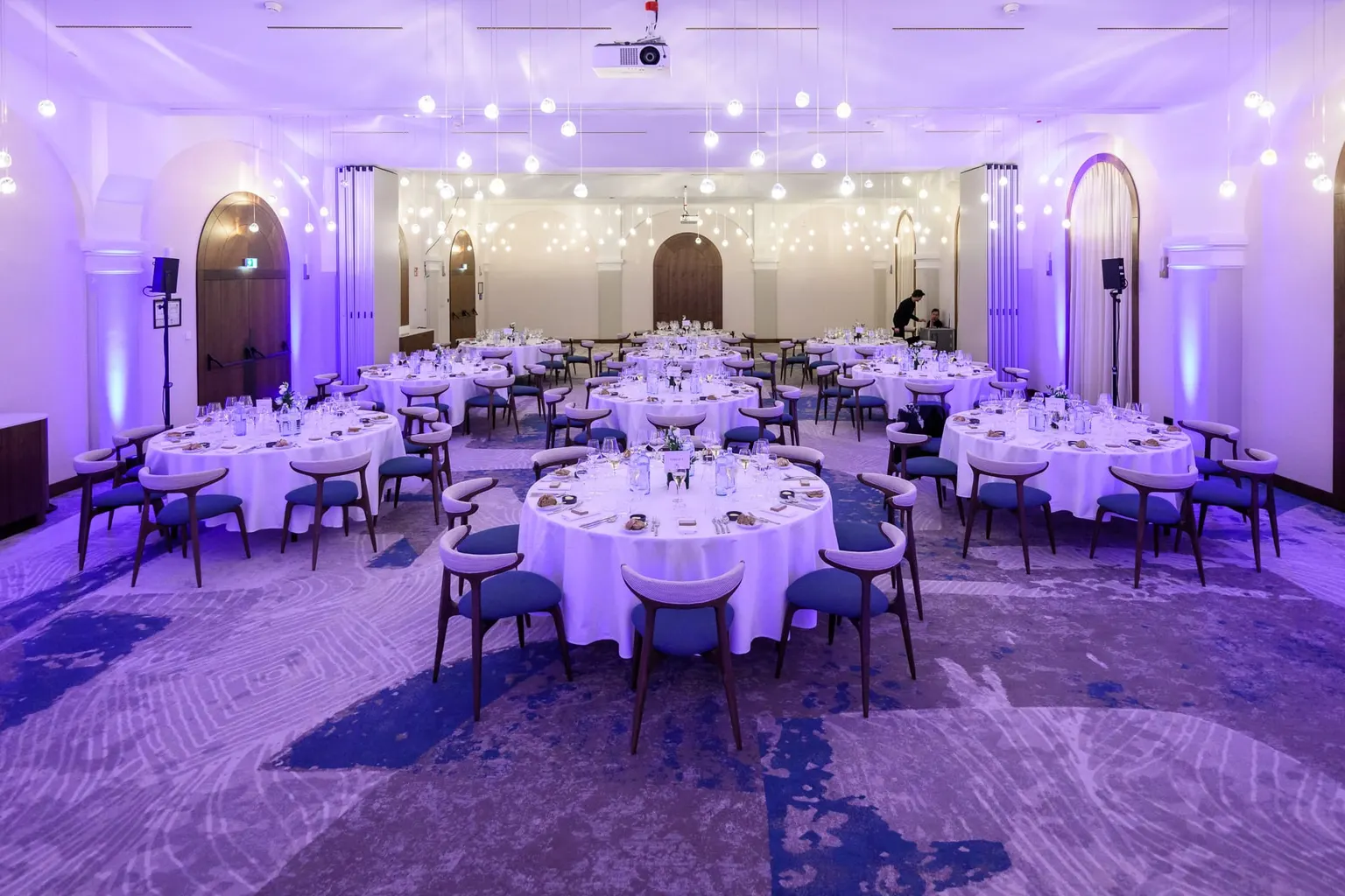 Ballsaal mit festlich gedeckten runden Tischen in violettem Licht für die HelmsBriscoe Konferenz
