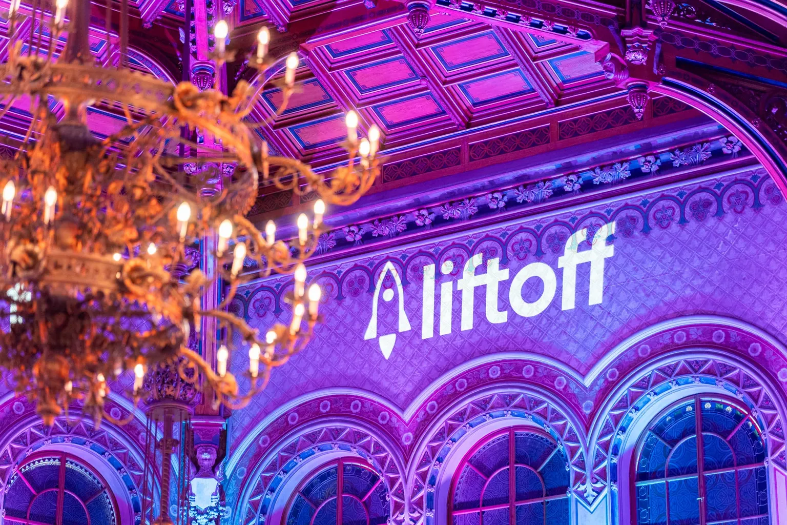 Prunkvoller Festsaal mit Kronleuchter und violett projiziertem Liftoff Logo