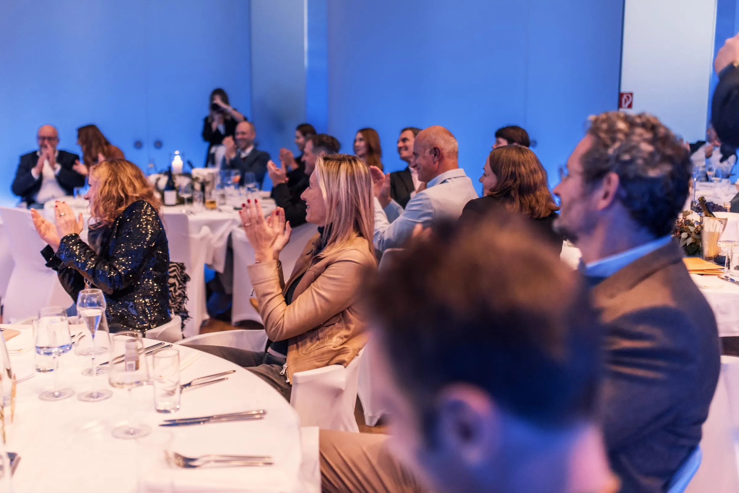 Gäste an festlich gedeckten Tischen in einem hellen Saal mit blauem Licht