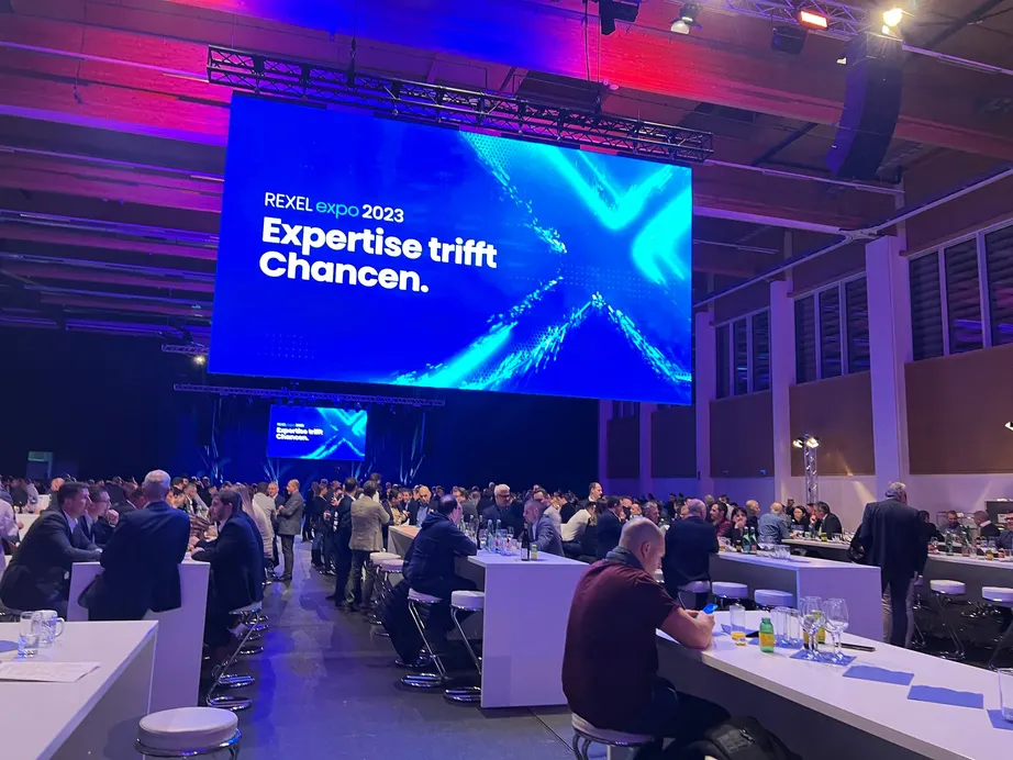 Messehalle der REXEL expo mit großer LED-Wand und Publikum